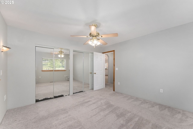 unfurnished bedroom featuring carpet flooring, a ceiling fan, and two closets