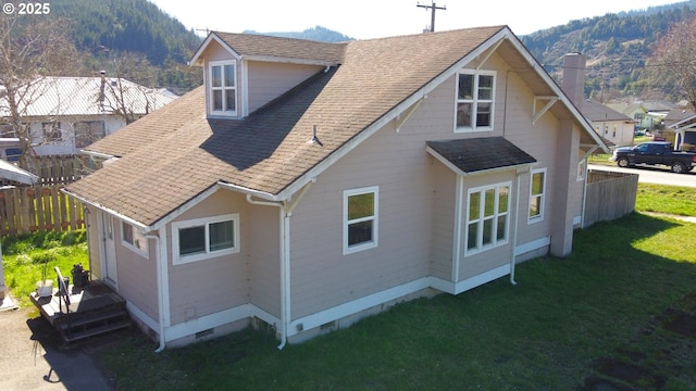 back of property featuring fence, roof with shingles, crawl space, a lawn, and a mountain view