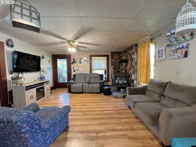 living room featuring light wood-style floors, a wood stove, a drop ceiling, and ceiling fan