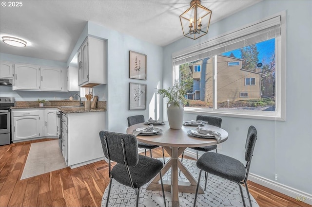 dining space with wood-type flooring, sink, and a notable chandelier