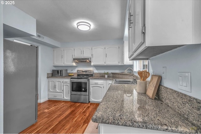 kitchen with sink, white cabinetry, appliances with stainless steel finishes, dark stone counters, and light hardwood / wood-style floors