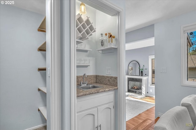 bar featuring sink, light stone counters, white cabinets, and light hardwood / wood-style floors