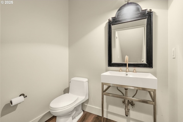 half bathroom with wood finished floors, toilet, baseboards, and a sink
