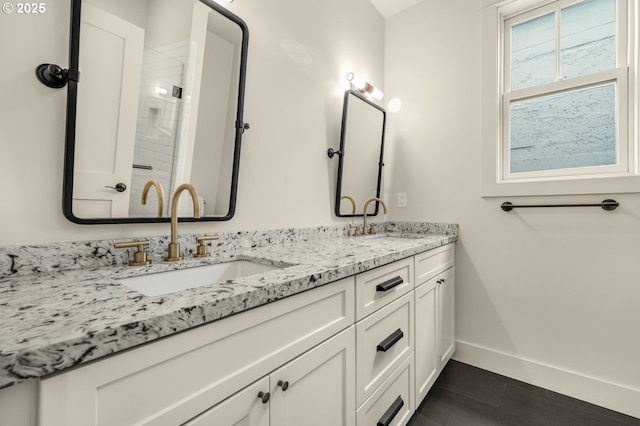 bathroom with baseboards, double vanity, and a shower with shower door