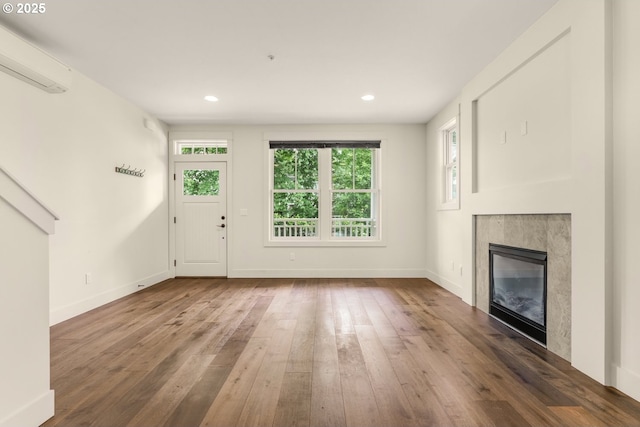 unfurnished living room featuring a wall mounted AC, hardwood / wood-style floors, a fireplace, baseboards, and recessed lighting