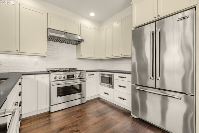 kitchen with high quality appliances, under cabinet range hood, dark countertops, backsplash, and recessed lighting