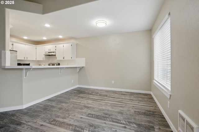 kitchen with visible vents, dark wood-type flooring, baseboards, under cabinet range hood, and a breakfast bar area