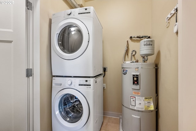 laundry area with light tile patterned flooring, stacked washing maching and dryer, and water heater