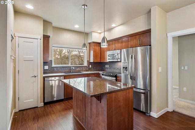 kitchen featuring a center island, sink, stainless steel appliances, dark stone countertops, and decorative light fixtures