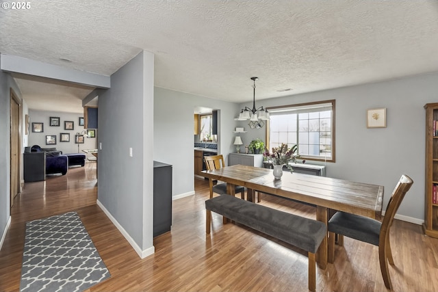 dining space featuring baseboards, a textured ceiling, wood finished floors, and a notable chandelier