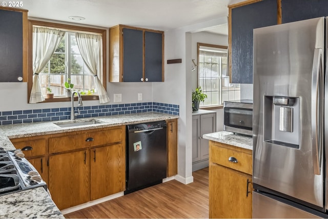 kitchen with stainless steel appliances, a sink, light wood-style floors, backsplash, and brown cabinetry