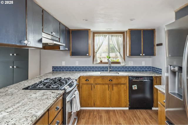 kitchen featuring brown cabinetry, light wood-style flooring, stainless steel appliances, under cabinet range hood, and a sink