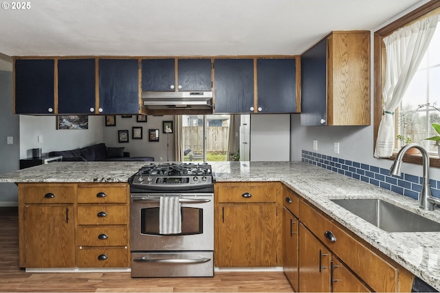 kitchen featuring under cabinet range hood, a sink, stainless steel gas range oven, and light stone countertops