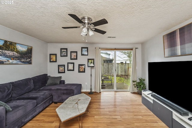 living area with ceiling fan, a textured ceiling, and light wood-style floors