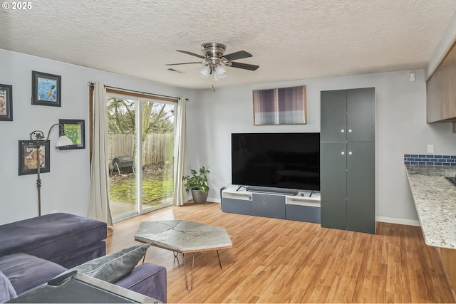 living room featuring a ceiling fan, light wood-type flooring, a textured ceiling, and baseboards