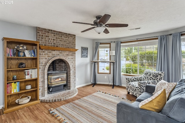 living room featuring a wood stove, light wood finished floors, visible vents, and a textured ceiling