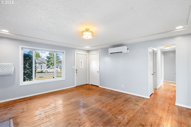 spare room featuring a textured ceiling, a wall unit AC, and light hardwood / wood-style flooring