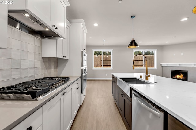 kitchen with backsplash, appliances with stainless steel finishes, white cabinets, a sink, and wall chimney exhaust hood