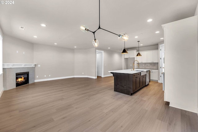 kitchen with white cabinets, open floor plan, stainless steel dishwasher, light wood-type flooring, and tasteful backsplash