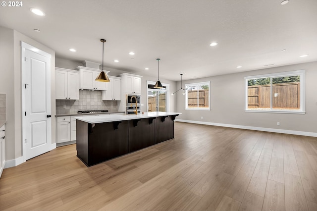 kitchen featuring an island with sink, white cabinets, light wood-style flooring, and decorative backsplash