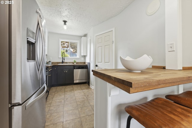 kitchen featuring appliances with stainless steel finishes, butcher block counters, a sink, a kitchen breakfast bar, and a textured ceiling
