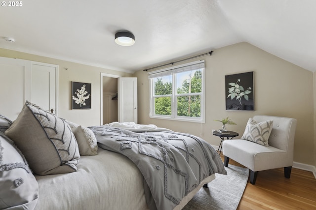 bedroom with wood finished floors, lofted ceiling, a closet, a walk in closet, and baseboards