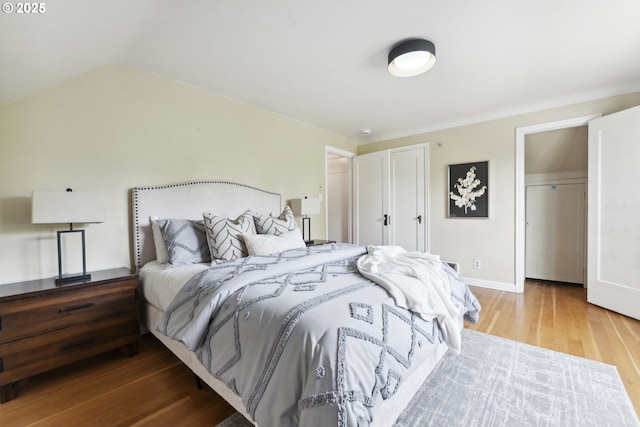 bedroom featuring wood finished floors, two closets, lofted ceiling, and baseboards
