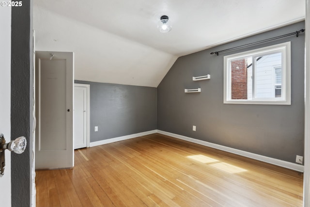 additional living space with light wood-style flooring, vaulted ceiling, and baseboards