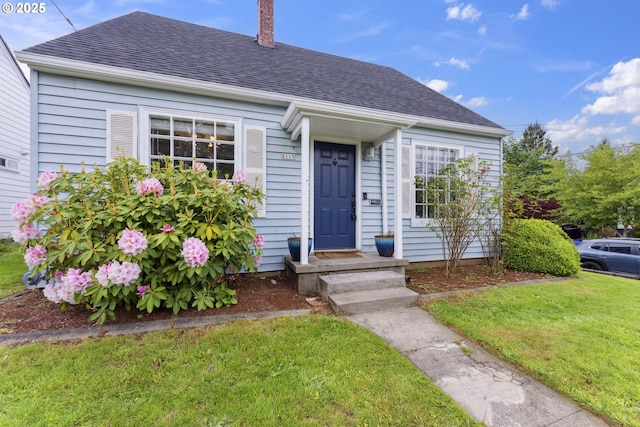 view of front of house featuring a shingled roof, a front yard, and a chimney