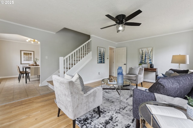 living area featuring stairway, ceiling fan, crown molding, baseboards, and wood finished floors