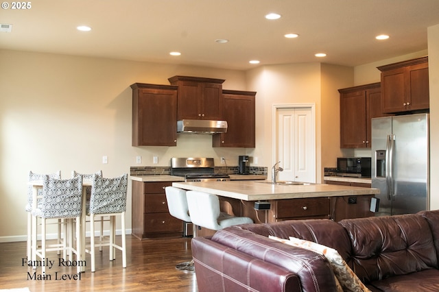 kitchen with recessed lighting, a sink, under cabinet range hood, appliances with stainless steel finishes, and open floor plan