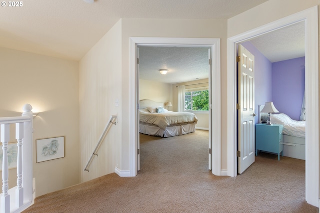 hallway featuring an upstairs landing, carpet floors, and a textured ceiling