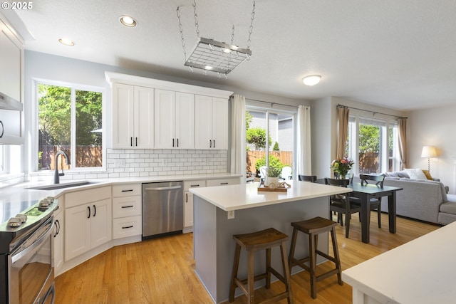 kitchen with stainless steel appliances, a sink, open floor plan, a kitchen island, and white cabinets
