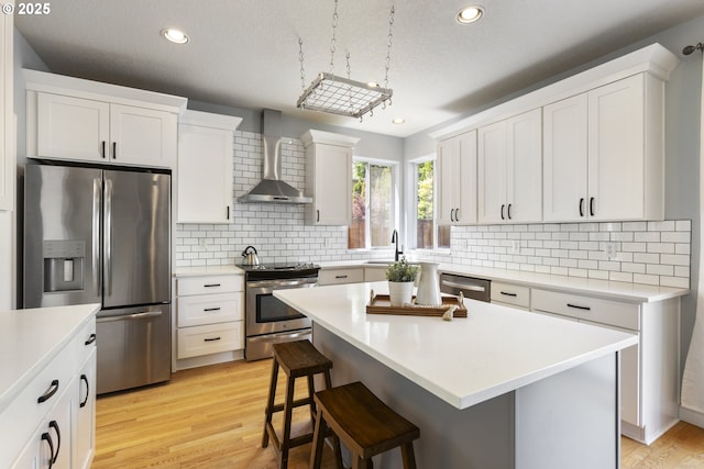 kitchen with appliances with stainless steel finishes, wall chimney range hood, decorative backsplash, white cabinets, and a kitchen bar