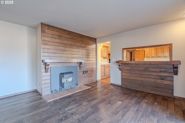 unfurnished living room with dark hardwood / wood-style floors, wood walls, and a wood stove