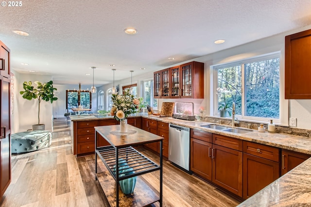 kitchen with sink, hanging light fixtures, light wood-type flooring, stainless steel dishwasher, and light stone countertops