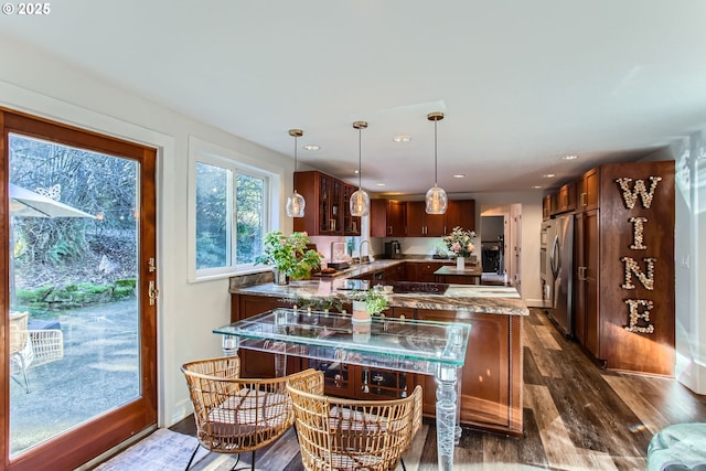 kitchen with sink, stainless steel refrigerator, hanging light fixtures, dark hardwood / wood-style floors, and light stone countertops