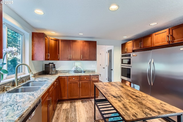 kitchen with sink, light hardwood / wood-style flooring, light stone countertops, and appliances with stainless steel finishes