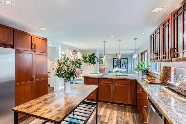 kitchen with pendant lighting, stainless steel appliances, light stone counters, light hardwood / wood-style floors, and kitchen peninsula