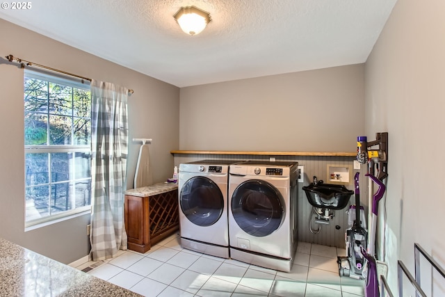 clothes washing area with independent washer and dryer, a textured ceiling, and light tile patterned flooring