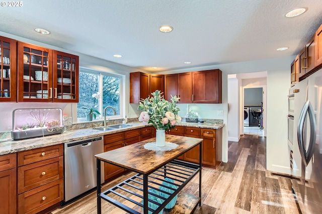 kitchen with sink, light hardwood / wood-style flooring, stainless steel appliances, light stone countertops, and washer and dryer