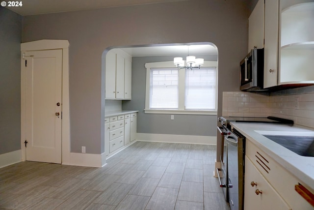 kitchen with pendant lighting, white cabinets, appliances with stainless steel finishes, tasteful backsplash, and a chandelier