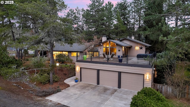 view of front of house featuring a chimney, concrete driveway, fence, a balcony, and a garage