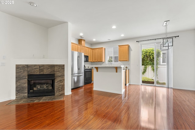 9234 SW Cascara Ln, Tualatin, OR 97062 - kitchen with black appliances, a breakfast bar area, open floor plan, wood finished floors, and recessed lighting