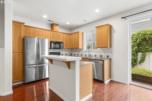 9234 SW Cascara Ln, Tualatin, OR 97062 - kitchen featuring appliances with stainless steel finishes, a center island, tile countertops, a sink, and dark wood-type flooring