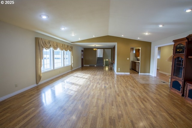 unfurnished living room featuring stairs, vaulted ceiling, wood finished floors, and baseboards