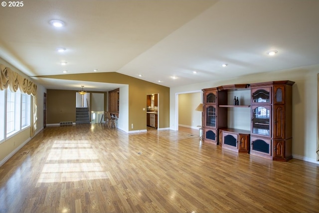 unfurnished living room featuring baseboards, stairway, vaulted ceiling, and wood finished floors