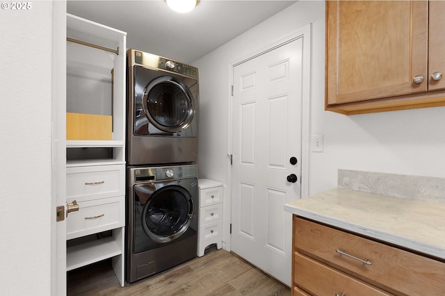 laundry area featuring cabinets, light hardwood / wood-style flooring, and stacked washer and clothes dryer