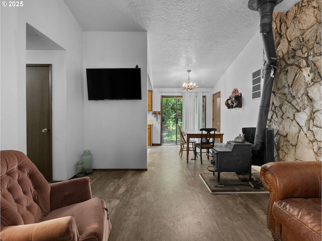 living area with a wood stove, a chandelier, a textured ceiling, and wood finished floors