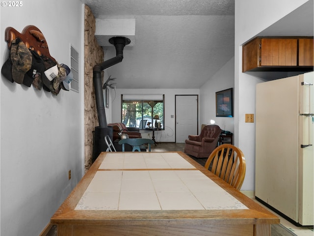 dining area featuring a wood stove, a textured ceiling, and vaulted ceiling